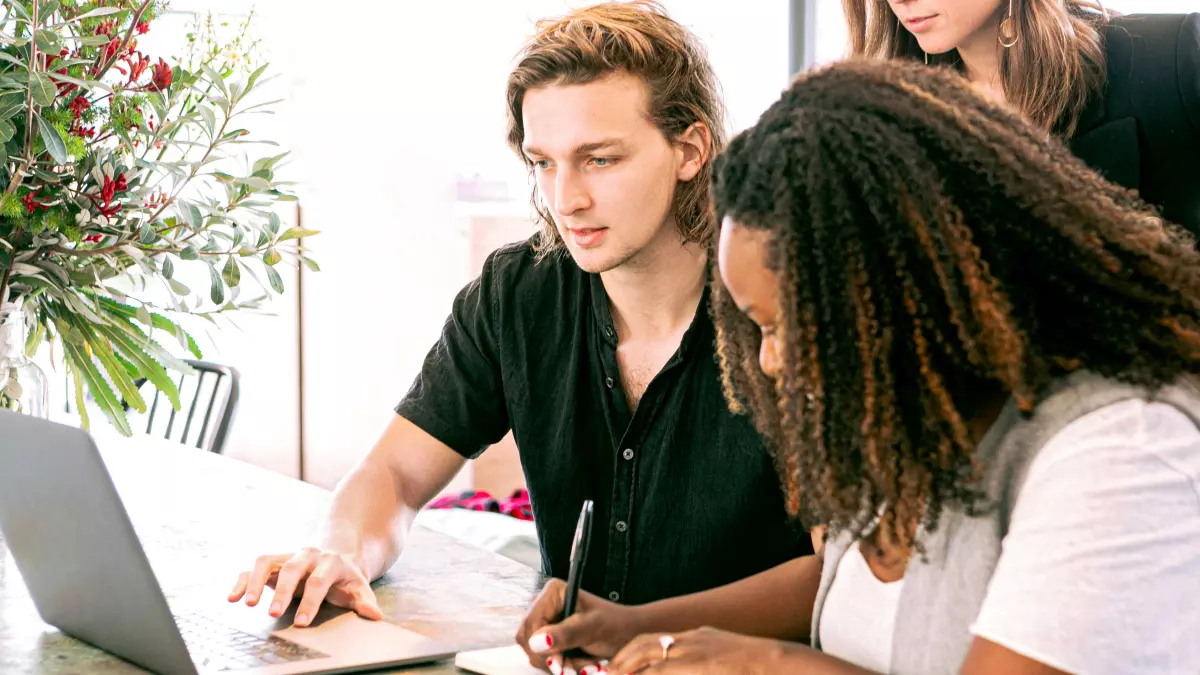 A group of people working on a project together, with a laptop and a notebook in the foreground.